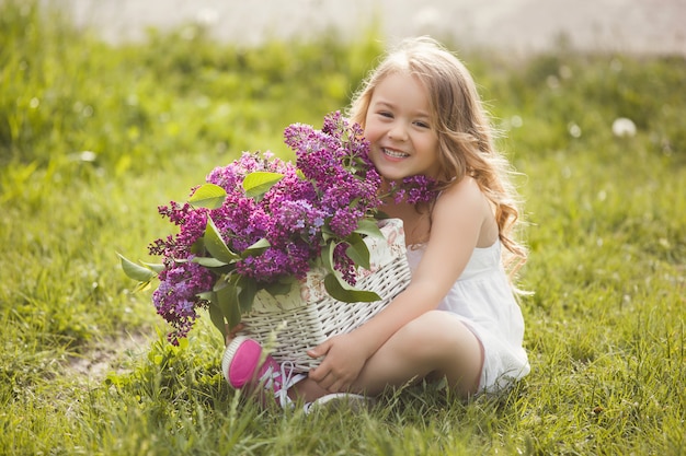 Śliczna mała dziewczynka outdoors z wiosen kwiatami. Ślicznotka z letnim bukietem bzu.