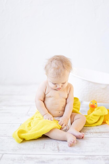 Śliczna mała dziewczynka pod żółtym ręcznikiem w łazience po kąpieli lub umyciu, koncepcja higieny dziecka