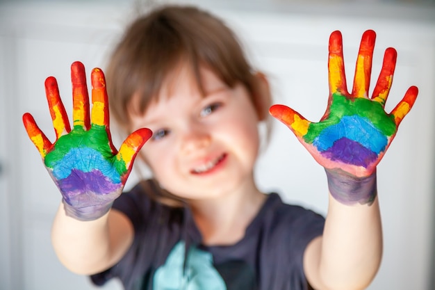 Śliczna mała dziewczynka pokazująca ręce z namalowaną na nich tęczą