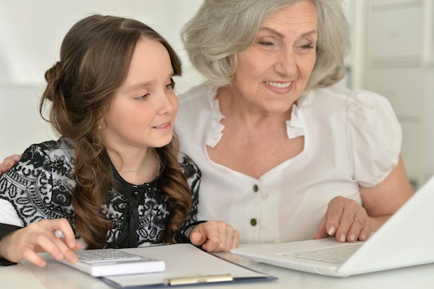 Śliczna mała dziewczynka robi pracę domową z babcią przy użyciu komputera