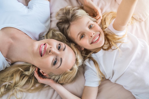 Śliczna mała dziewczynka robi selfie z matką leżąc w łóżku i relaksując się