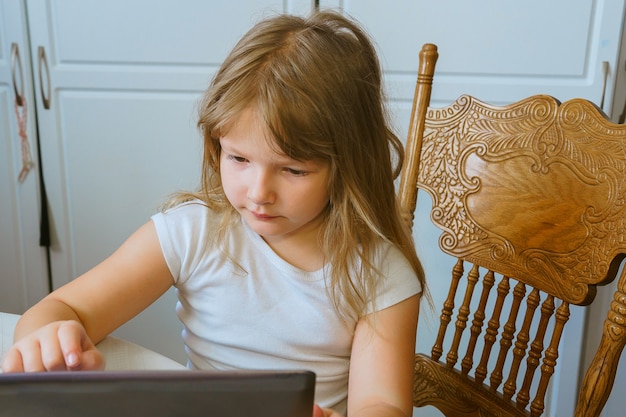 Śliczna mała dziewczynka siedzi pod ścianą i korzysta z komputera typu tablet