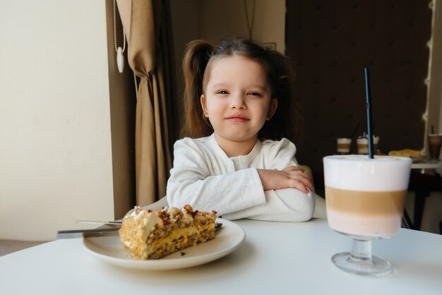 Śliczna Mała Dziewczynka Siedzi W Kawiarni I Patrzeje Zbliżenie Ciasto I Kakao. Dieta I Prawidłowe Odżywianie.