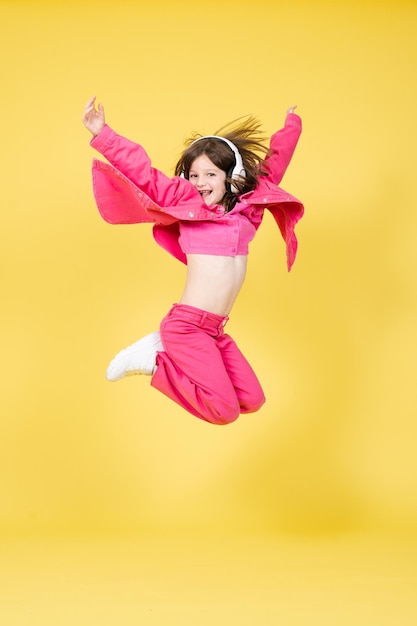 Śliczna mała dziewczynka skacze wysoko i tańczy podczas słuchania muzyki na słuchawkach