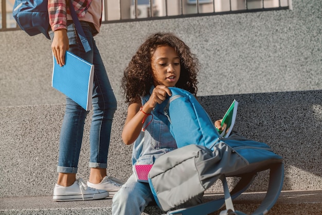 Śliczna mała dziewczynka składa swój szkolny plecak na zewnątrz