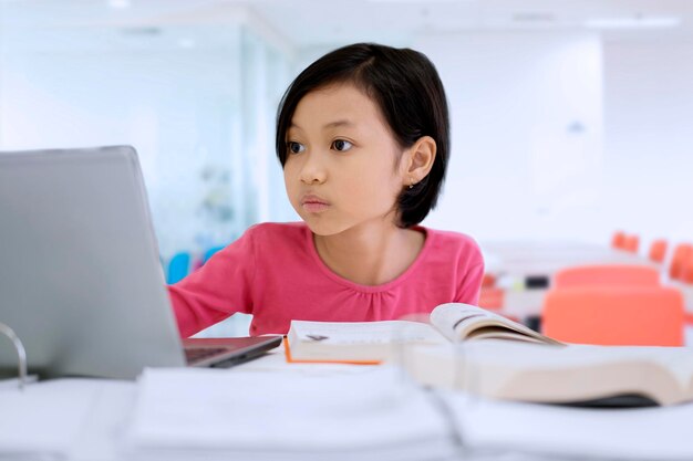 Śliczna mała dziewczynka studiuje z laptopem w klasie