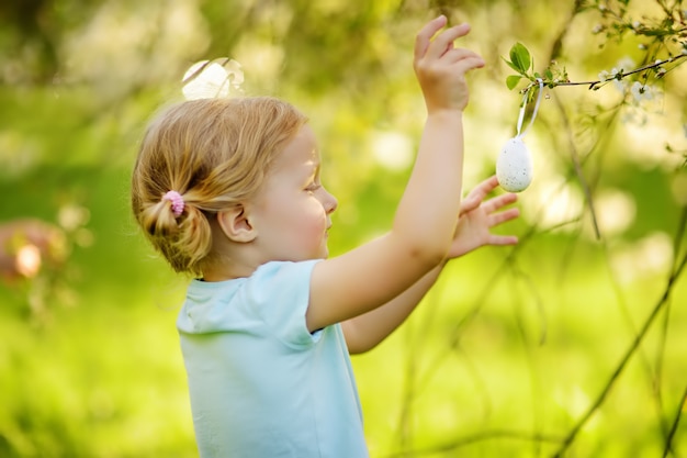 Śliczna Mała Dziewczynka Tropi Dla Easter Jajka Na Gałęziastym Kwiatonośnym Drzewie.