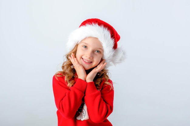 śliczna mała dziewczynka w czerwonym swetrze i kapeluszu Mikołaja na białym tle. Koncepcja świąteczna, miejsce na tekst