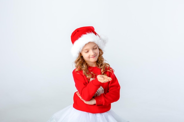 śliczna mała dziewczynka w czerwonym swetrze i kapeluszu Mikołaja na białym tle. Koncepcja świąteczna, miejsce na tekst