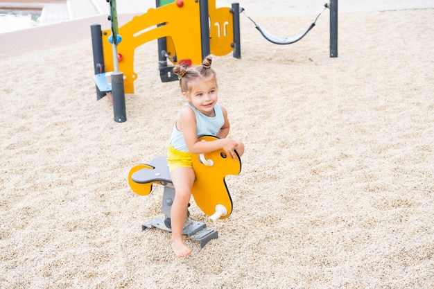 śliczna mała dziewczynka w kolorowe ubrania bawiące się na placu zabaw w letni dzień
