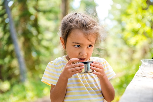 śliczna mała dziewczynka w letnim lesie trzymająca filiżankę herbaty i uśmiechnięta