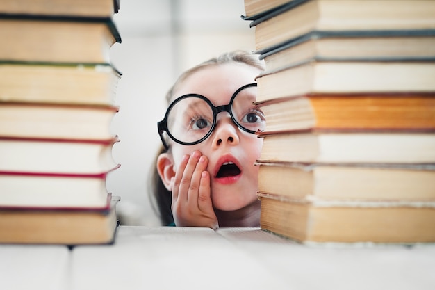 Śliczna mała dziewczynka w okrągłych okularach przestraszona zbyt wieloma książkami, które musi przeczytać