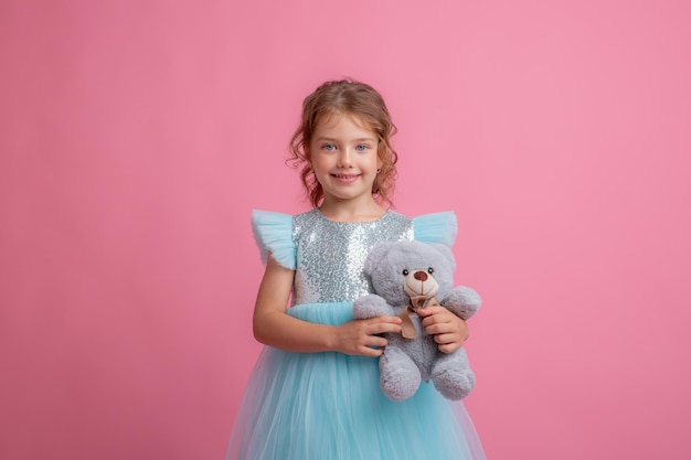 Śliczna mała dziewczynka w pięknej sukience trzyma misia na różowym tle
