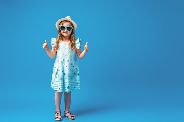 Zdjęcie Śliczna mała dziewczynka w pozach sukienka, kapelusz i okulary przeciwsłoneczne