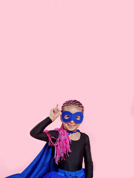 Śliczna mała dziewczynka w stroju superbohatera, trzymając go za rękę i wskazując na różową przestrzeń. Skopiuj miejsce.