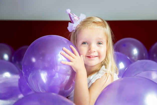 Śliczna mała dziewczynka w stylowej sukni świętuje urodzinowego dzień z purpurowymi balonami