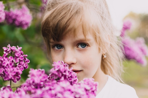 Śliczna mała dziewczynka w sukience śmiejąca się w wiosennym parku w pobliżu bzu dziecko pachnie bzem