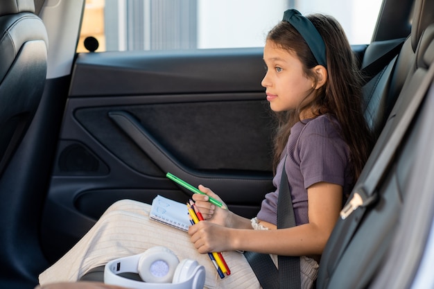 Śliczna mała dziewczynka z kredkami czeka na rodziców w samochodzie