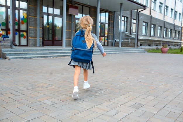 Śliczna mała dziewczynka z plecakiem biega z powrotem do szkoły.