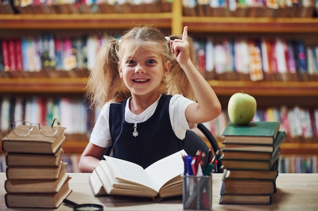 Śliczna mała dziewczynka z warkoczykami jest w bibliotece