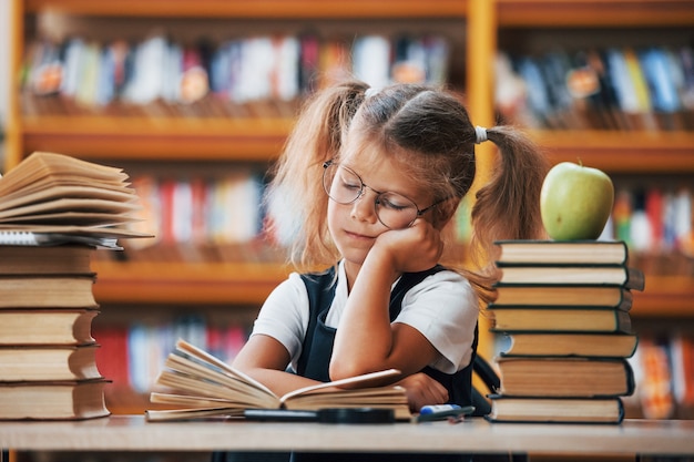 Śliczna mała dziewczynka z warkoczykami jest w bibliotece