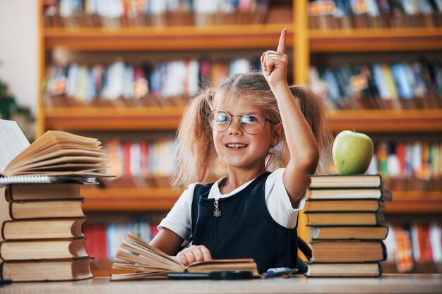 Śliczna mała dziewczynka z warkoczykami jest w bibliotece