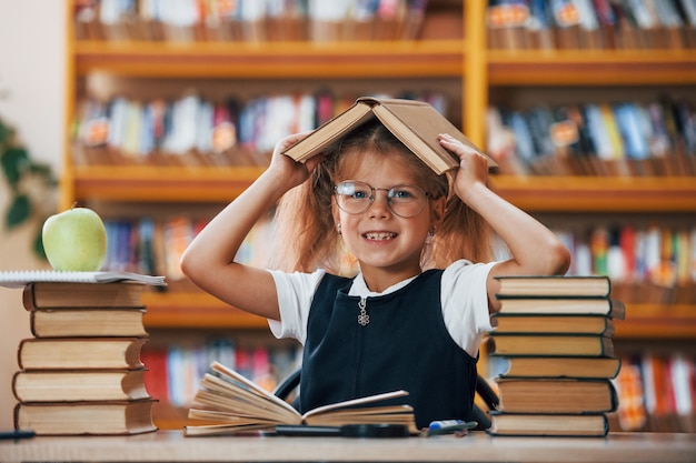 Śliczna mała dziewczynka z warkoczykami jest w bibliotece