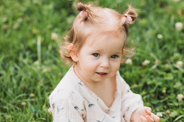 śliczna mała dziewczynka z zabawną fryzurą siedzi na kwitnącym zielonym trawniku w parku Lifestyle