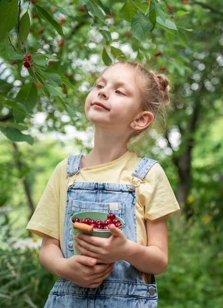 Śliczna mała dziewczynka zbiera wiśnię z drzewa w wiśniowym ogrodzie