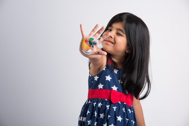 Śliczna mała indyjska dziewczyna pokazująca swoje kolorowe dłonie lub dłonie drukujące lub malujące lub grające w holi festiwal z kolorami, odizolowane na białym tle