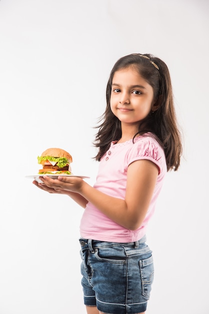 Śliczna mała indyjska lub azjatycka dziewczyna je burgera na białym tle