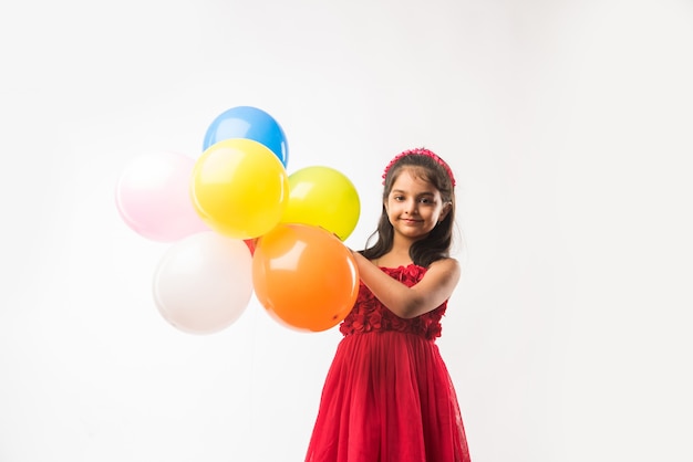 Śliczna mała indyjska lub azjatycka dziewczyna z kolorowymi balonami lub gubbary w hindi, na białym lub czerwonym tle