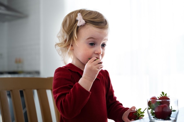 Śliczna mała kaukaska blond dziewczynkamaluch prettyadorable niemowlę jedzące truskawki ze stołu w