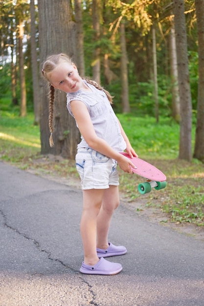 Śliczna mała preteen dziewczyna pozuje z deskorolką w pięknym parku w słoneczny dzień