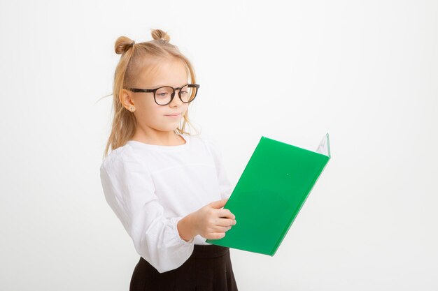 Śliczna mała uczennica w okularach mundurków szkolnych trzymająca książki na białym tle