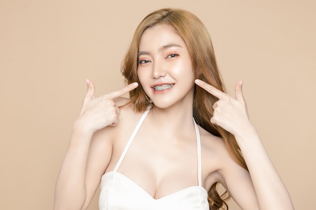 Śliczna młoda azjatycka kobieta nosząca szelki czuje się szczęśliwa z czystą, świeżą skórą na białym tle kremowym