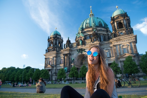 Śliczna młoda dziewczyna siedzi przed berlińską katedrą o pięknym zachodzie słońca i je czekoladę