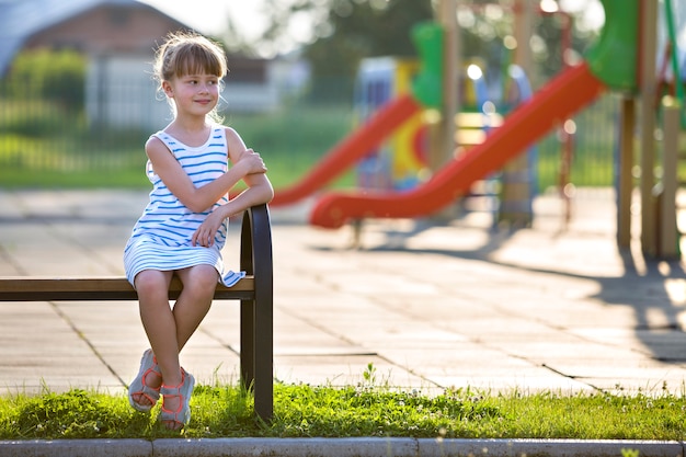 Śliczna młoda dziewczyna siedzi samotnie na ławce w boisko w pogodnym letnim dniu w krótkiej sukni.