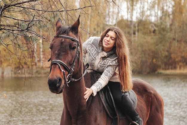 Śliczna młoda kobieta na koniu w jesiennym lesie nad jeziorem