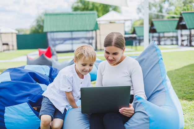 Śliczna młoda matka i syn patrzą na laptopa Szczęśliwa rodzina matka i syn odpoczywają w parku Kobieta na urlopie macierzyńskim