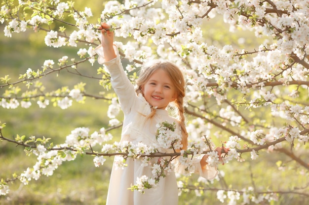 śliczna śmieszna dziewczynka w sukience na wiosnę w pobliżu kwitnącego drzewa śmieje się delikatna fotografia
