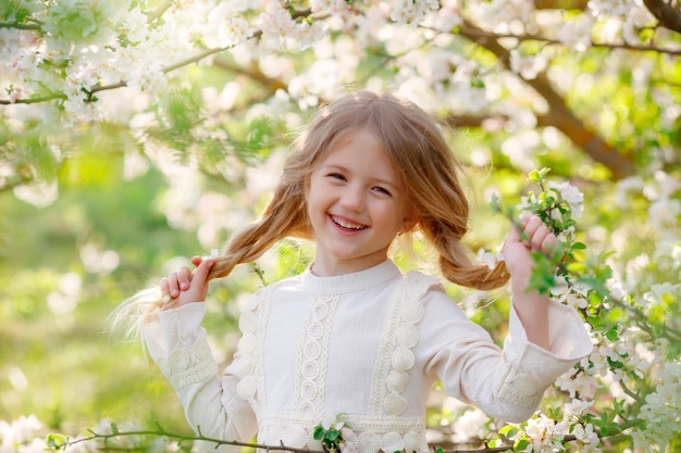 śliczna śmieszna dziewczynka w sukience na wiosnę w pobliżu kwitnącego drzewa śmieje się delikatna fotografia