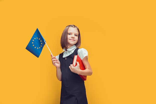 Śliczna uczennica trzymająca małą flagę unii europejskiej i książkę w ręku edukacja w koncepcji europy