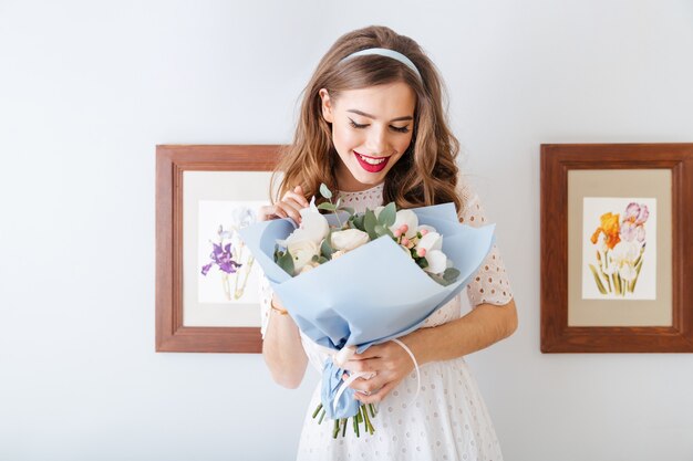 Śliczna urocza szczęśliwa młoda kobieta stojąca i patrząca na bukiet kwiatów