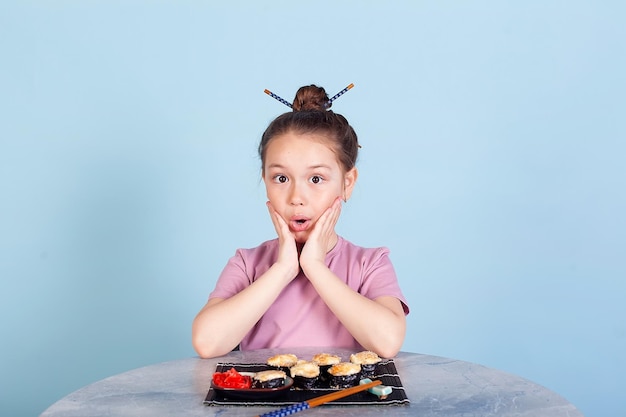 Śliczna uśmiechnięta dziewczynka z sushi na czerwonym tle Uczennica dziewczynka jedząca sushi i bułki koncepcja komercyjna