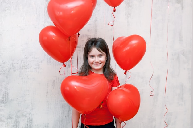 Zdjęcie Śliczna uśmiechnięta mała dziewczynka stoi wśród czerwonych balonów