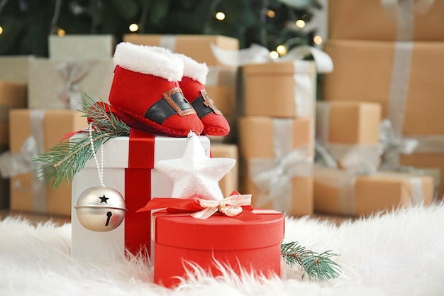 Śliczne buciki dla dziecka i pudełka na prezenty na futrzanym dywanie w udekorowanym pokoju na Boże Narodzenie
