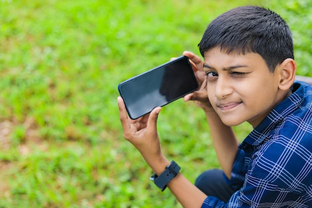 Śliczne indyjskie małe dziecko pokazuje smartfon z pustym ekranem