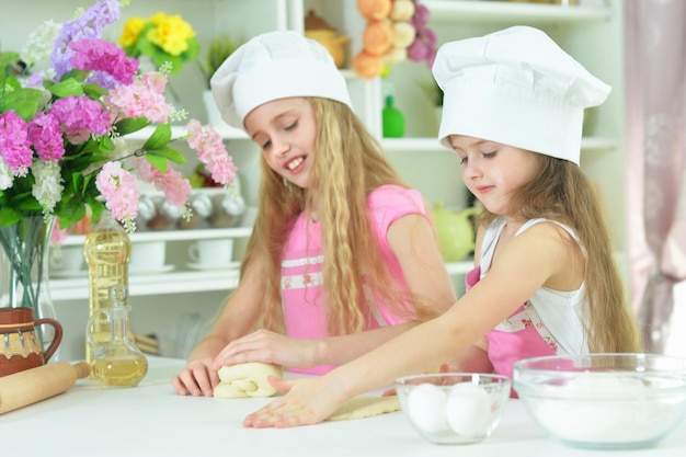Śliczne małe dziewczynki w czapkach szefów kuchni robią ciasto