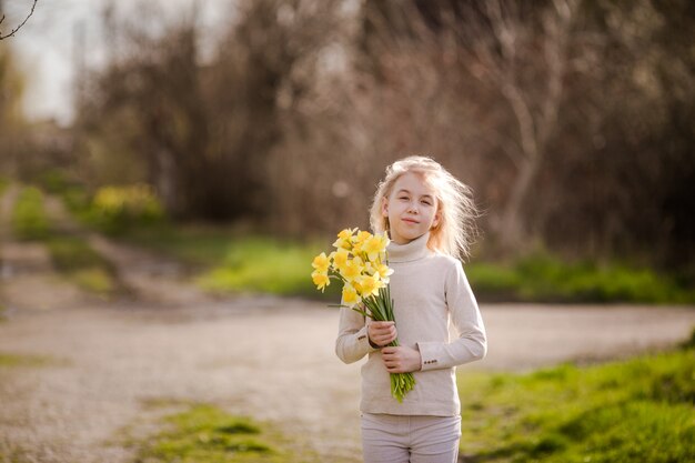 Ślicznej blondynki szczęśliwa mała dziewczynka z żółtymi daffodils w wiosna kraju